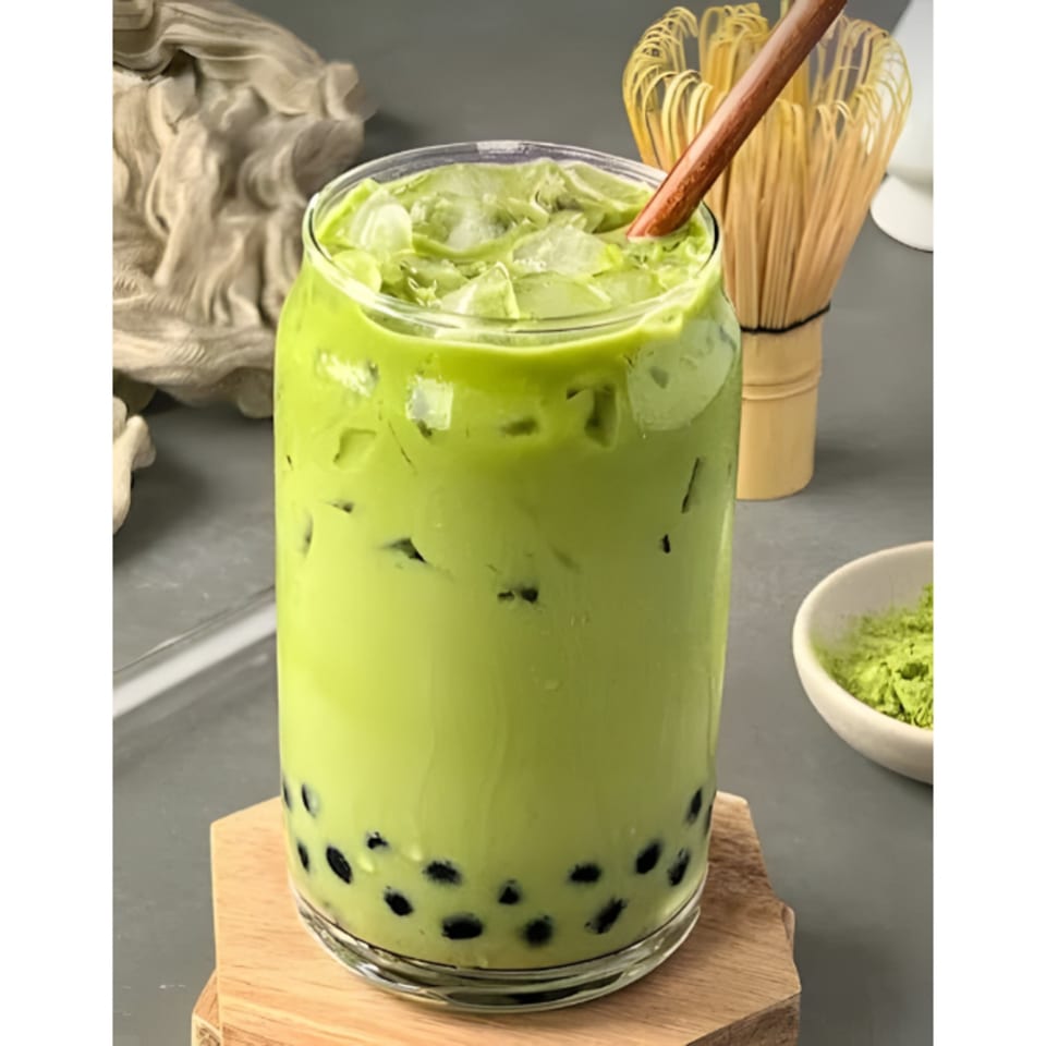 Iced matcha boba tea in a clear glass with a wooden straw, on a wooden coaster.