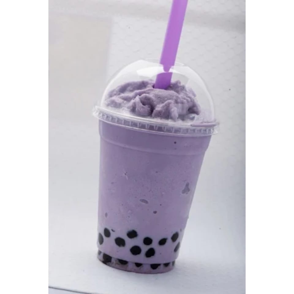 Purple taro bubble tea with black boba pearls and a purple straw in a clear plastic cup.