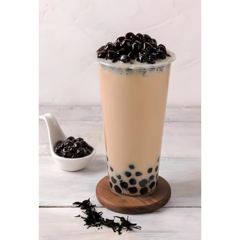 A tall glass of Vietnamese bubble tea with tapioca pearls on a wooden coaster.